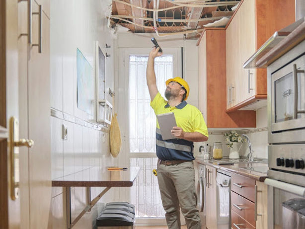 Home inspector shining a flashlight on exposed ceiling damage in a kitchen