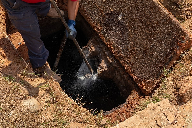 Worker clearing a blocked underground septic line with a spade